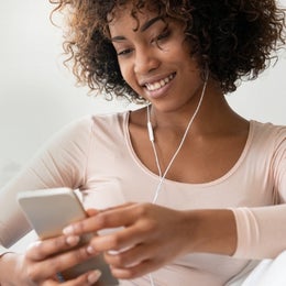 Image of a woman listening to music on headphones while using her cell phone.