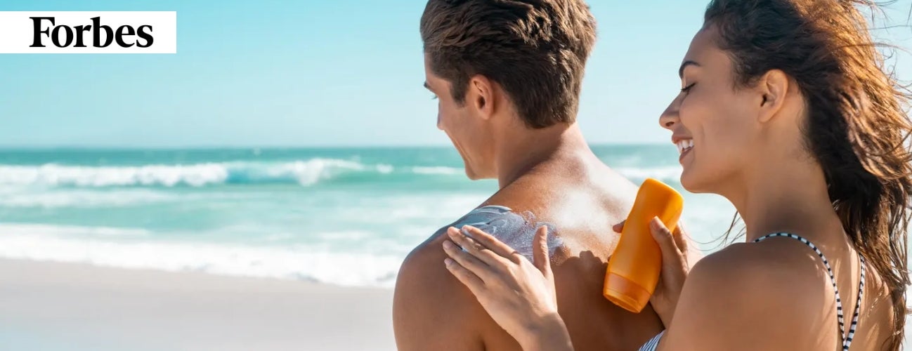 Image of a woman applying sunscreen to a man’s back on the beach. 