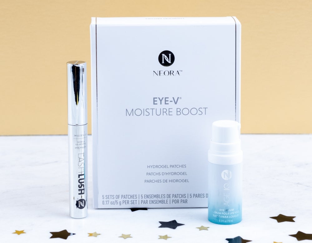 Neora’s LashLush tube, Eye-V Moisturize Hydrogel Eye Patches, and Age IQ Eye Serum are grouped together. They rest on a white marble table with glitter stars surrounding them. And text that says “save 15%.