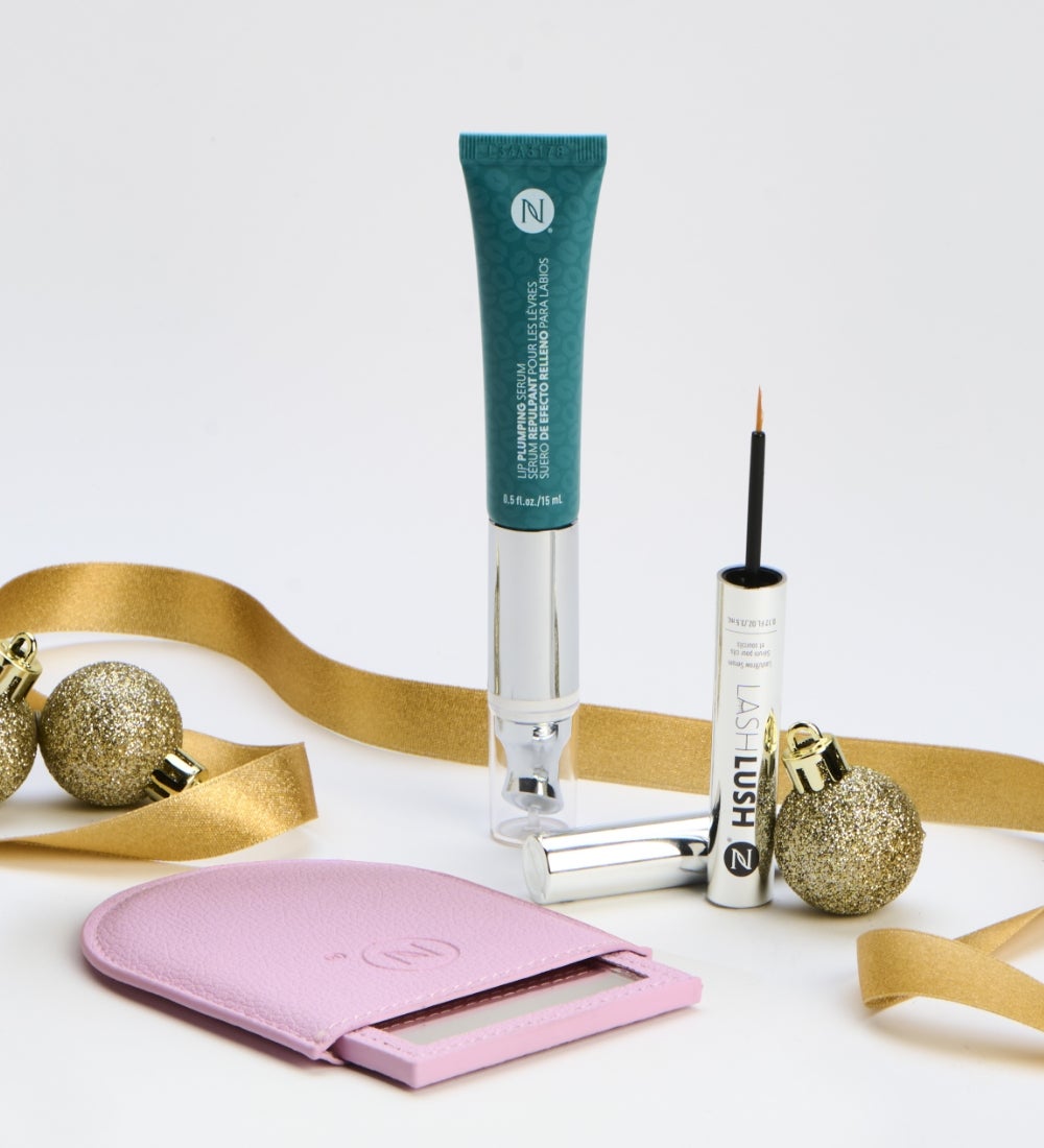  Free Gift! A bottle of Age IQ Day Cream, two IllumaBoost bottles, a Facial Treatment Tube, and a Lip Oil container are surrounded by festive, gold ribbon and ornaments.
