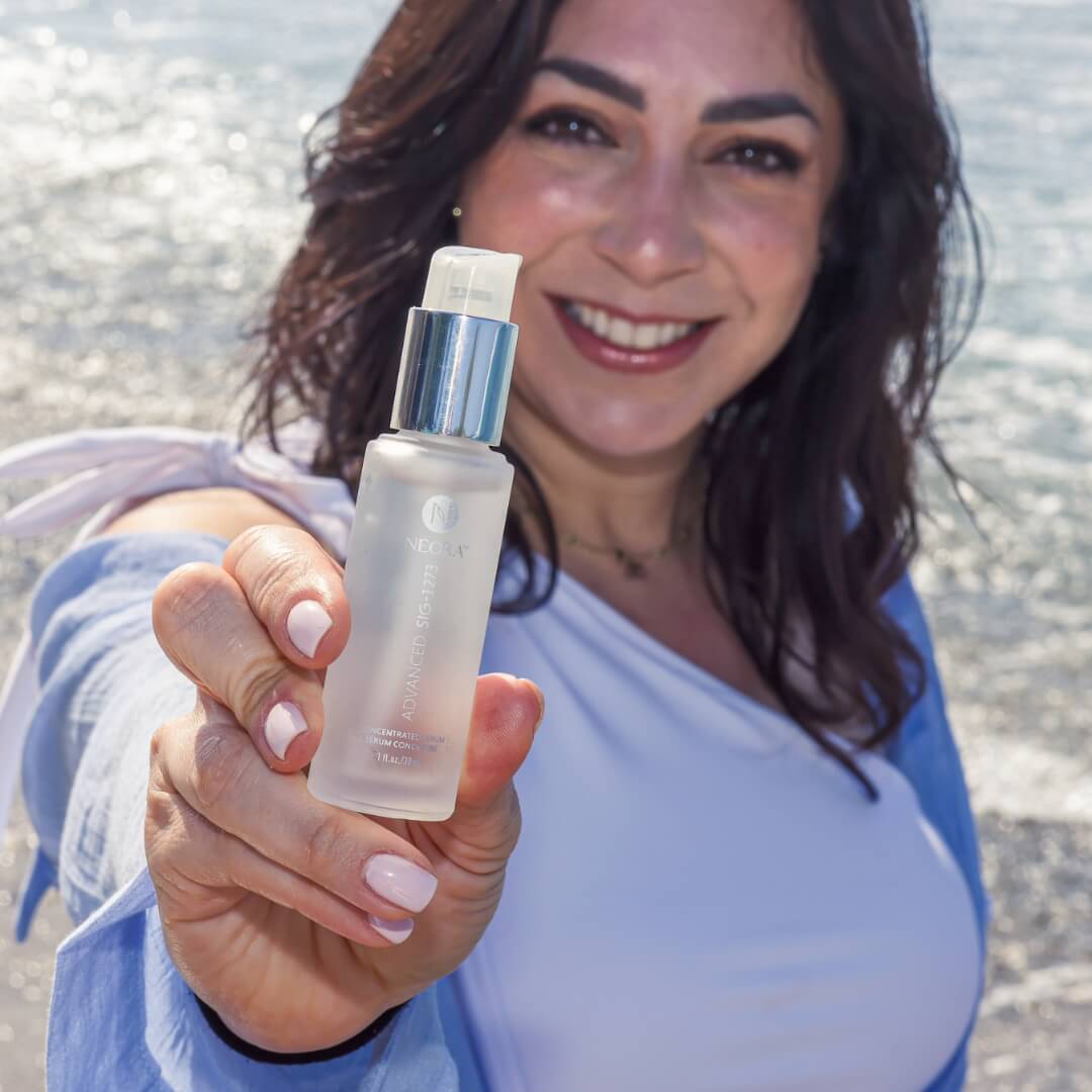 A woman holding up a bottle of Neora's Sig Serum