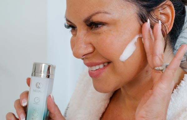 A woman applying the Age IQ Day Cream on her face in a bathroom.