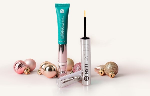 A tube of LashLush and Lip Plumping Serum surrounded by festive ornaments on a white background.