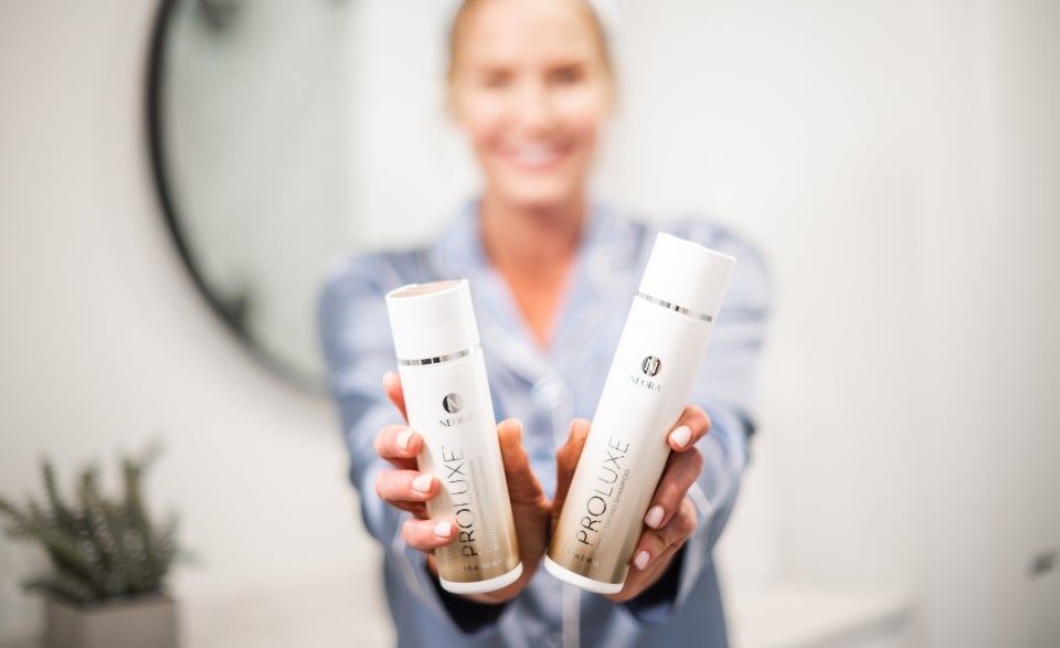 Lifestyle shot of a woman holding up the ProLuxe Shampoo and Conditioner bottles.