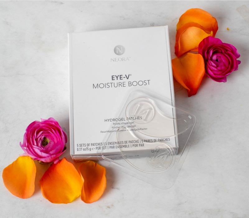 Parches de hidrogel Eye-V™ Moisture Boost de Neora sobre un mesón junto a pétalos de rosa